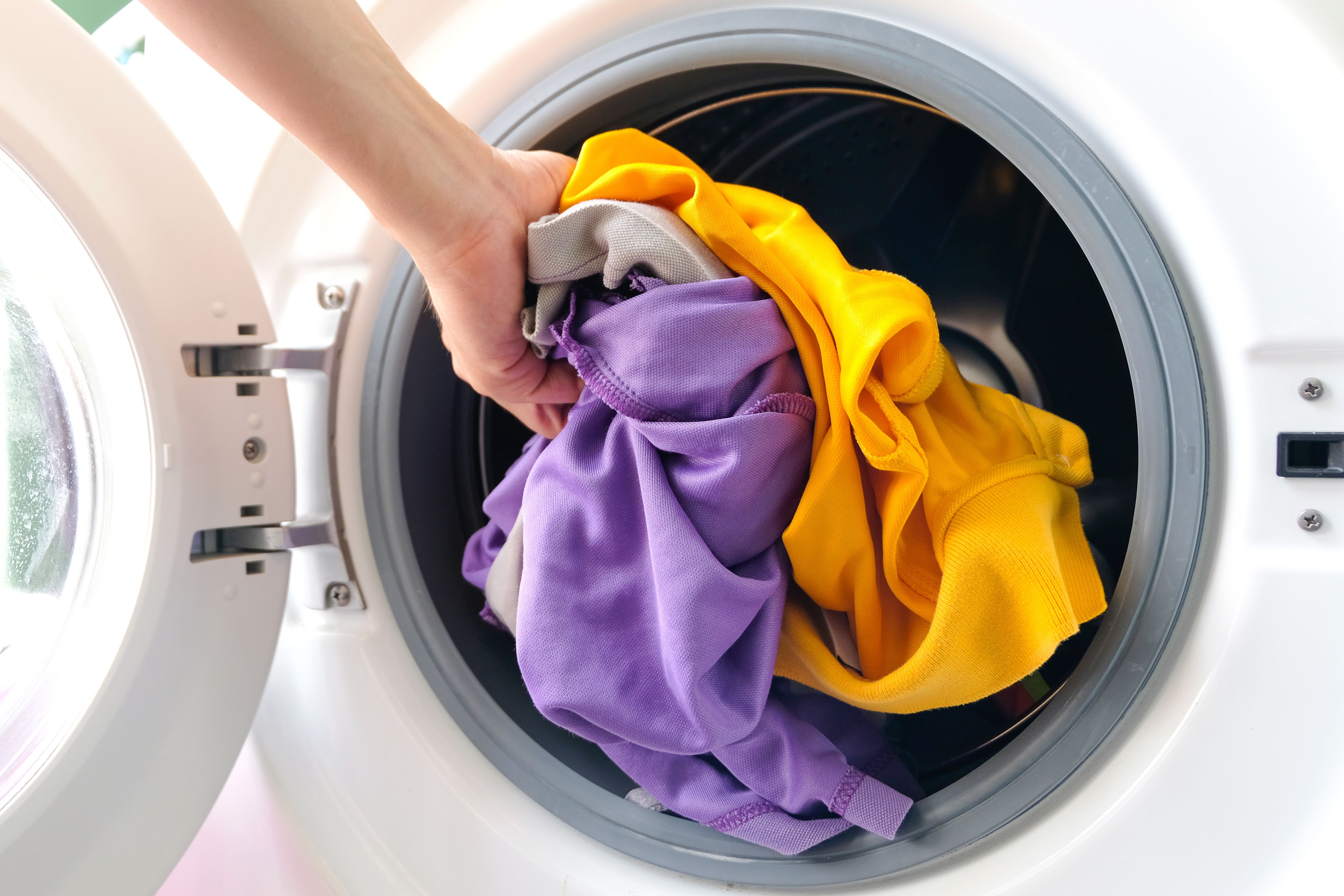 Man places printed clothes into washing machine – care tip for personalized T-shirts and hoodies
