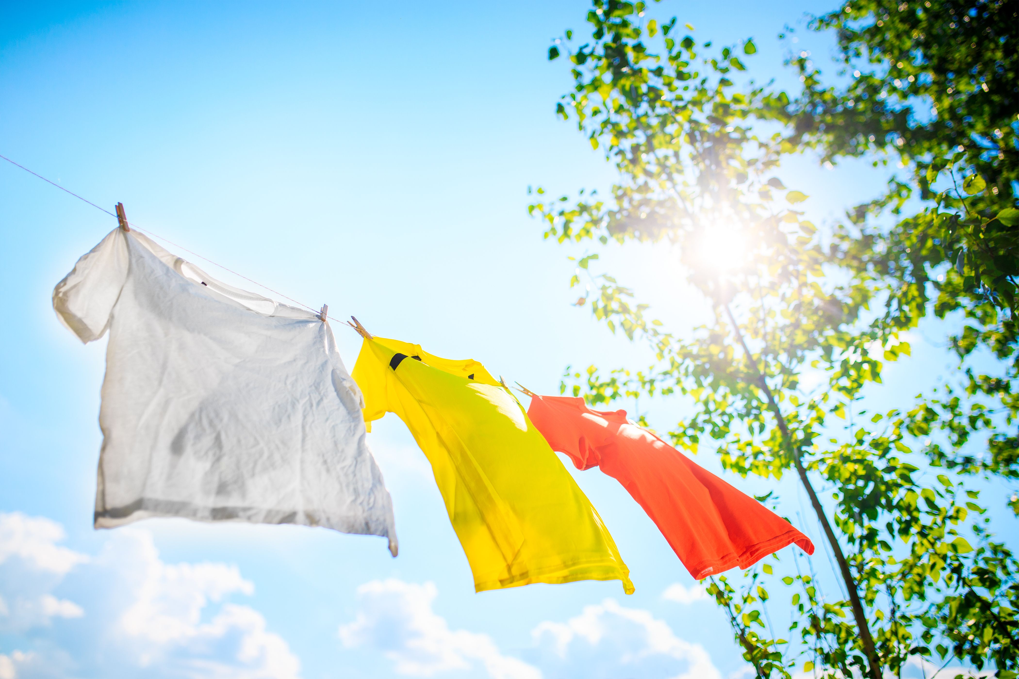 Three T-shirts hang on a line under blue sky – gentle drying for personalized clothes