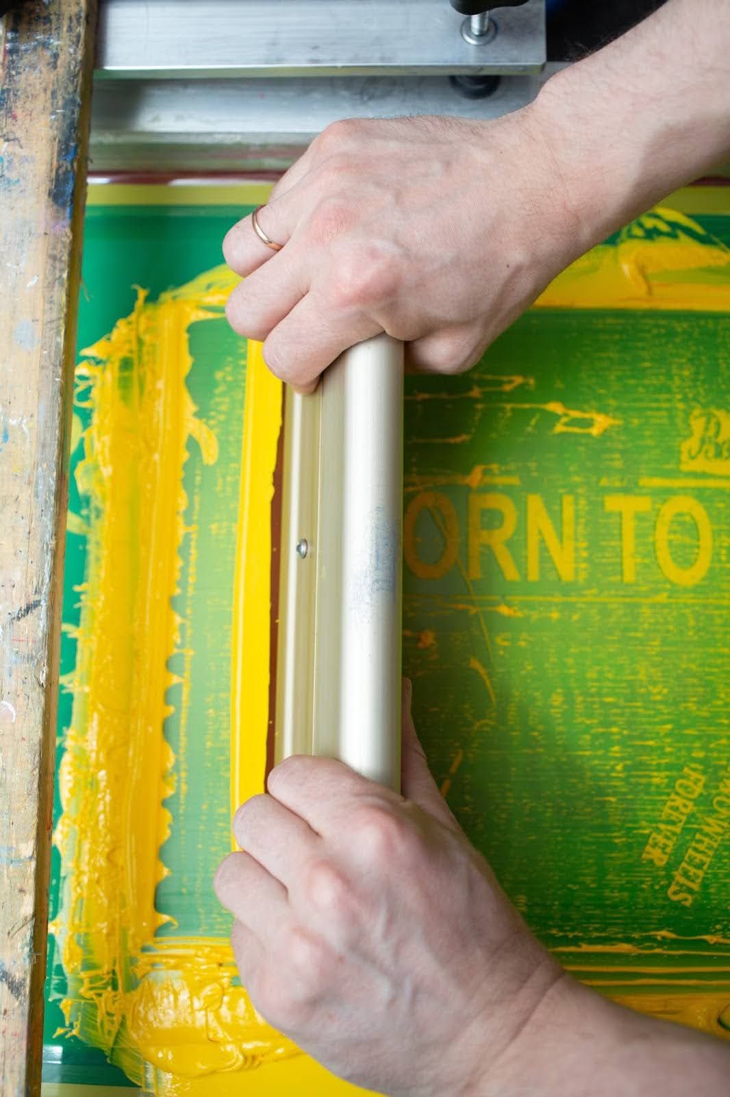 Screen printing process: Yellow paint is precisely applied to a T-shirt using a stencil and squeegee in a textile print shop