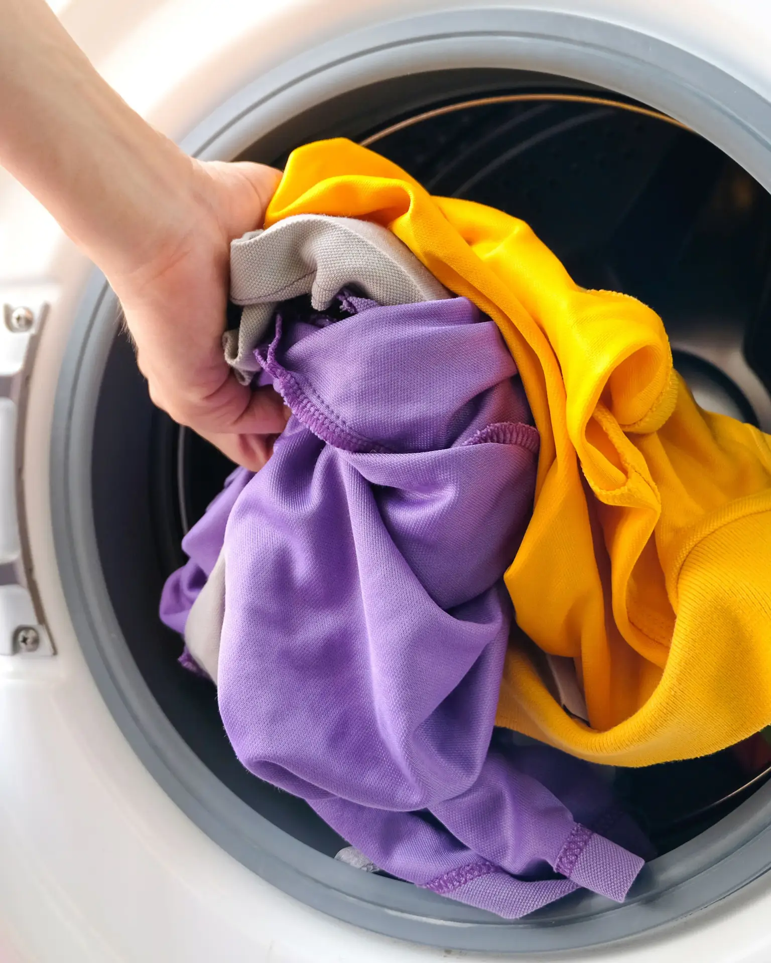 Mann legt bedruckte Kleidung in Waschmaschine – Pflegehinweis für personalisierte T-Shirts und Hoodies