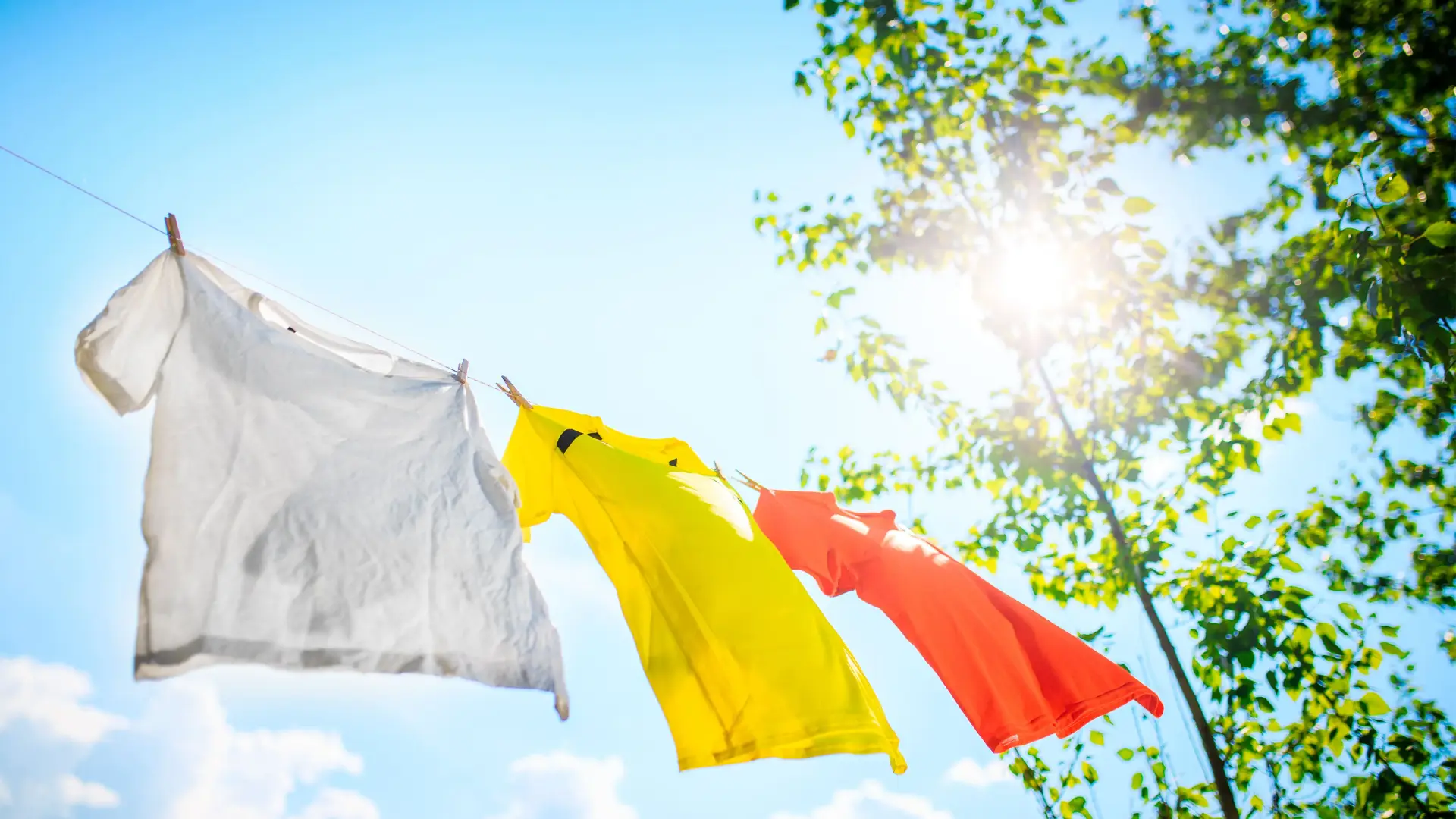 Drei T-Shirts hängen an Leine vor blauem Himmel – schonende Trocknung personalisierter Kleidung