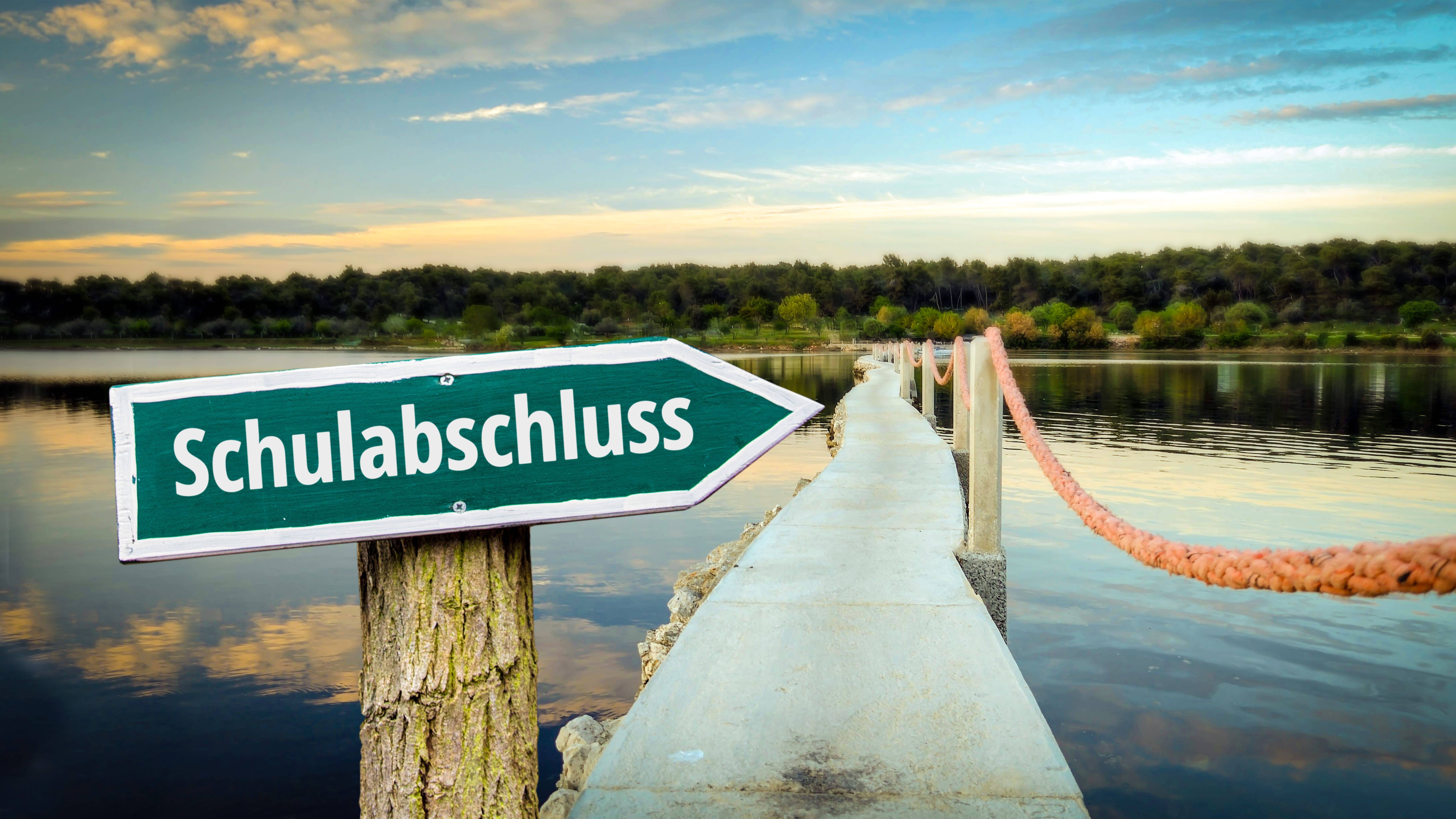 Ein Steg am See mit Schild „Schulabschluss“ im Vordergrund – Symbolbild. Abschluss-Outfits und Abi-Pullis online gestalten mit KI