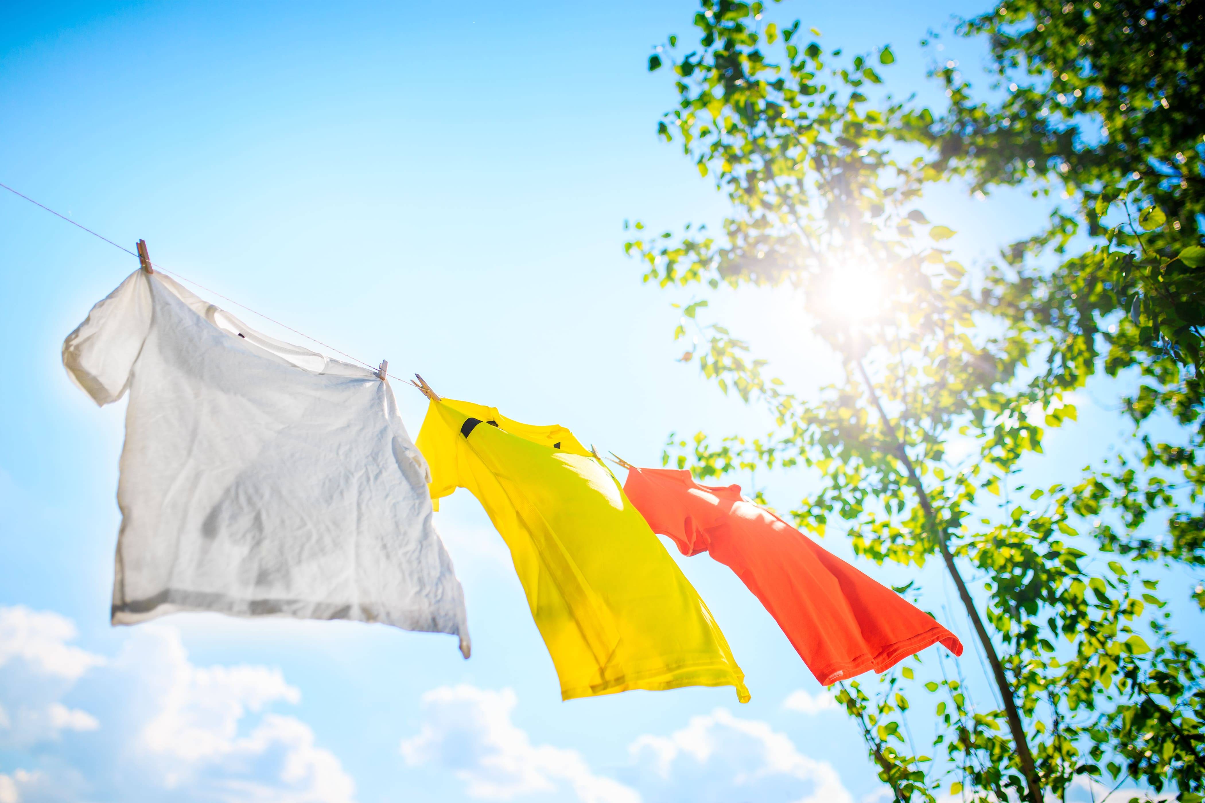 Drei T-Shirts hängen an Leine vor blauem Himmel – schonende Trocknung personalisierter Kleidung