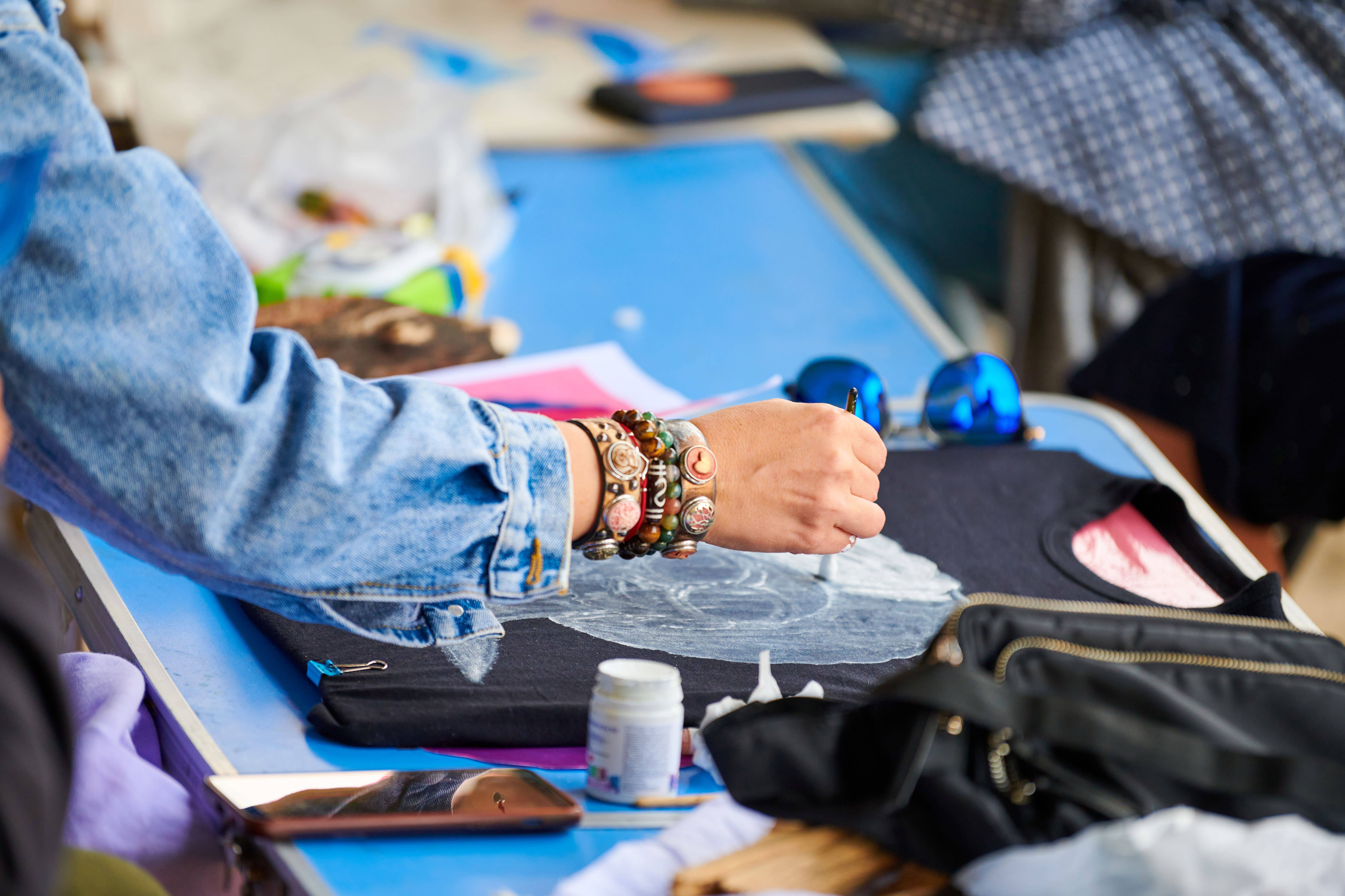 Eine Frau gestaltet in einem Workshop ein schwarzes T-Shirt per Hand mit Pinsel und Textilfarbe – abstraktes Design im DIY-Stil